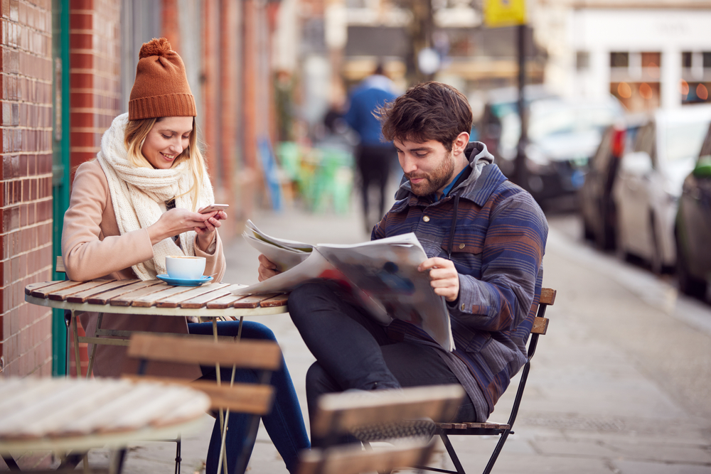 people at a table out doors man reading a newspaper. place advertising in the midwest