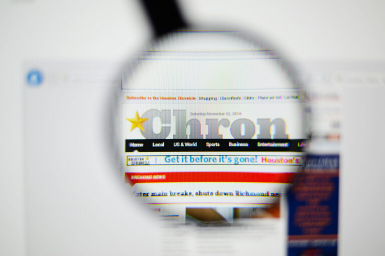 Houston Chronicle homepage on a monitor screen through a magnifying glass. PLace ads in Houston or across Texas