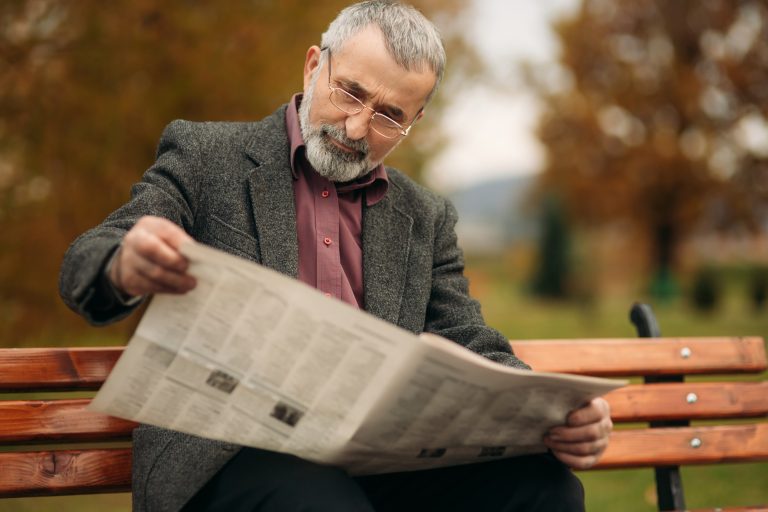 senior man reading the newspaper and reading public service announcements