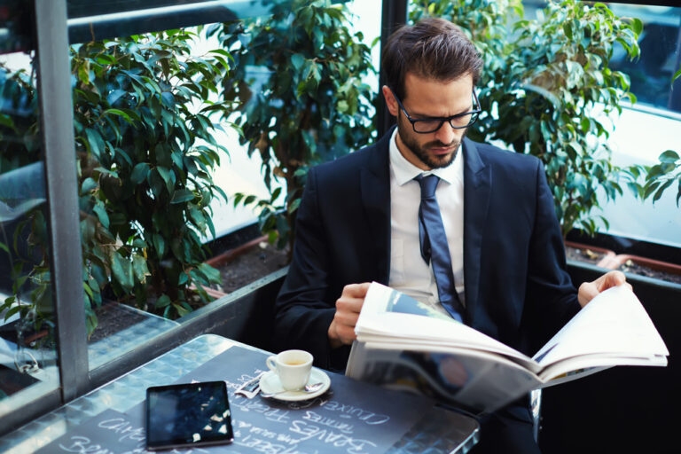 Man in a suit reading a newspaper the benefits of run of paper advertising are immense