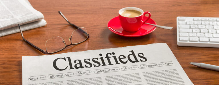 Classified advertising newspaper on a desk with a copy cup and glass displaying Classified advertising page